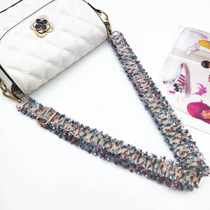 Detail of white quilted crossbody bag with golden flower clasp and colorful tweed strap
