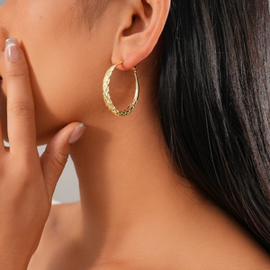 Close-up of a model wearing a gold twisted hoop earring with a metallic woven texture