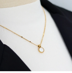 Detail of 18K gold-plated necklace with a white shell round pendant on a black blazer