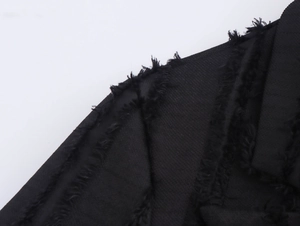 Close-up of black double-breasted coat fabric featuring detailed texture and fringe trim