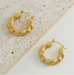 Detail of twisted 18k gold earrings on textured stone showcasing fine braided design