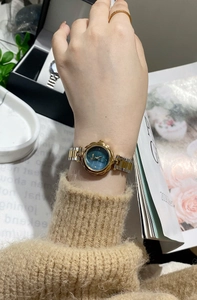 Close-up of a small gold and silver steel watch with a blue dial worn on a female wrist