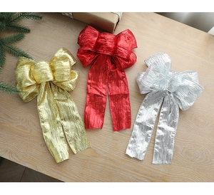Three large glitter fabric Christmas bows in gold, red, and silver on a wooden table