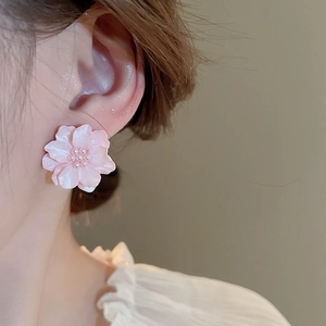 Dettaglio di orecchini a fiore rosa con perla centrale indossati da una modella