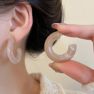 Detail of C-shaped apricot acrylic hoop earrings with a smooth resin texture and silver pins