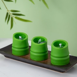 Detailed view of three green bamboo-shaped scented candles on a dark ceramic tray