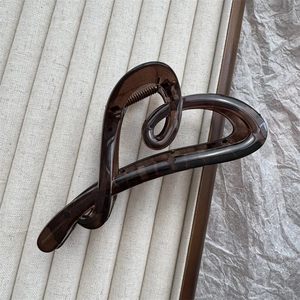 Detail of dark brown heart-shaped hair claw clip on neutral textured fabric background