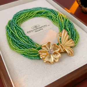 Detail of beaded necklace featuring golden butterfly flower charm with sparkling rhinestones
