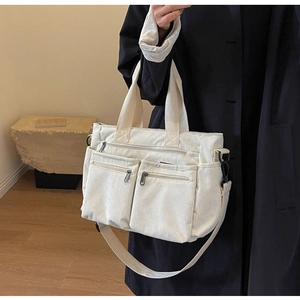 Detail of off-white corduroy tote bag showing front zipper pockets and ribbed texture