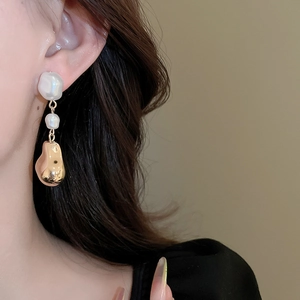 Gros plan d'une boucle d'oreille en métal doré et perle baroque portée par un mannequin