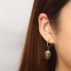 Close-up of gold snake earrings with green enamel inlay on earlobe of a model