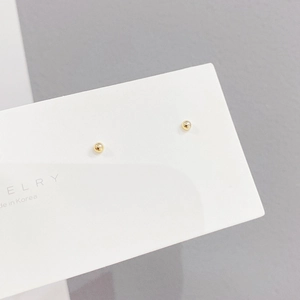 Close-up of golden ball stud earrings on a white display card in minimalist style