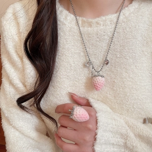 Close-up of a pink flocked strawberry necklace and ring set worn by a female model