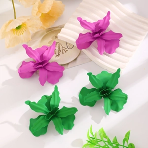 Detail showing oversized purple and green matte 3D flower earrings on a textured tray