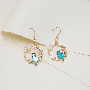 Close-up of golden wreath earrings featuring a blue enamel cat, stars and tiny flowers