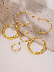 Detailed view of three pairs of PVD 18K gold-plated C-shaped hoop earrings on beige sandstone