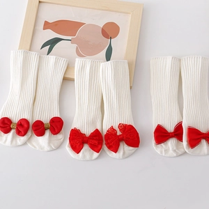 Three pairs of white cotton knit baby socks with decorative red bows on white background