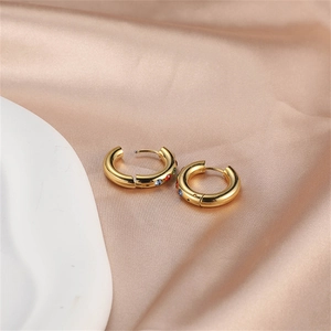 Detailed macro view of gold hoop earrings with multi-color zircon stones on beige silk