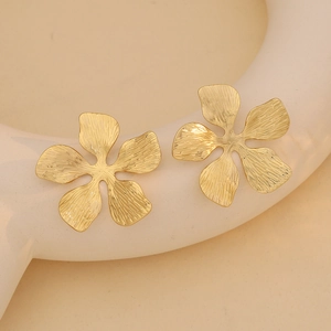 Macro detail of golden flower stud earrings with elegant brushed metal texture