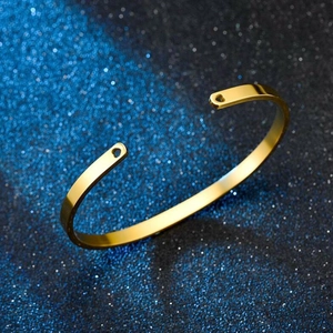 Polished gold stainless steel C-shaped open cuff bracelet on a starry dark background