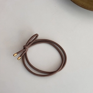 Détail d'un élastique à cheveux marron avec double brin et attache métallique dorée