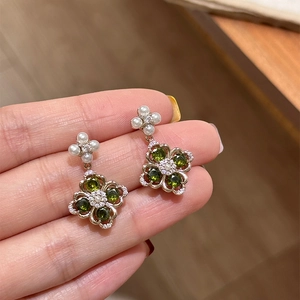 Macro shot of silver drop earrings featuring green zircon flowers and small white pearls