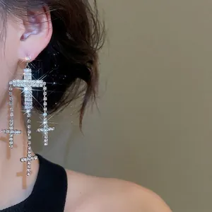 Sparkling silver cross tassel earrings with rhinestones on model in warm grey background