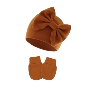 Detail of infant knit hat with large bow and matching mittens in caramel ribbed cotton