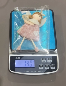 Weight measurement detail of pink plush angel Christmas tree ornament showing 14.0 grams