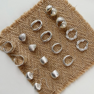 Collection of S925 sterling silver earrings with shells and pearls on jute background