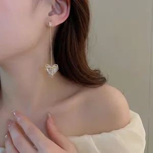 Eleganti orecchini pendenti dorati con cuore di zircone mostrati su una modella