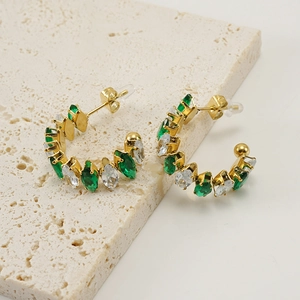 Detalle de pendientes en C dorados con circonitas verdes y blancas sobre piedra