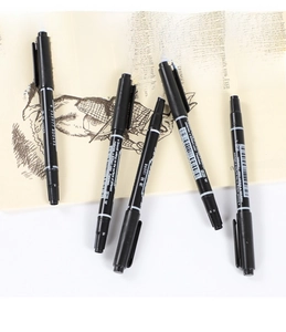 Close-up of five black dual-tip permanent markers on an open book for school and office