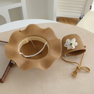 Detail of brown straw sun hat with wavy brim and matching floral woven shoulder bag