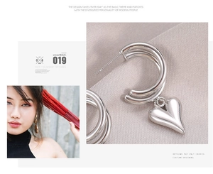 Dettaglio di orecchini a cuore in argento a forma di C indossati da una modella su raso