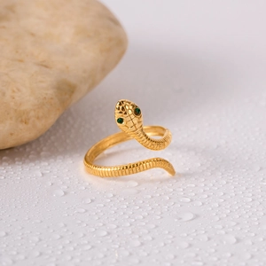 Macro shot of gold snake ring with green gem eyes and textured scales on wet surface