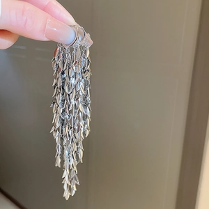 Detail of silver long fringe earrings with layered metallic leaf elements for women