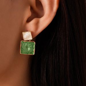 Detail view of a model wearing green and white geometric square earrings with gold trim