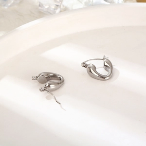 Close-up of silver irregular hoop earrings placed on a white texture plate in high detail