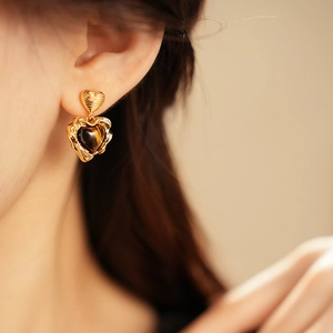 Detail of gold-plated heart earrings with tiger eye stone inlay worn by a model