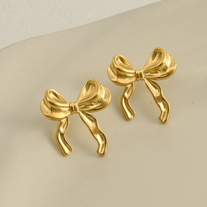 Macro shot of 18k gold plated stainless steel bow stud earrings on beige backdrop