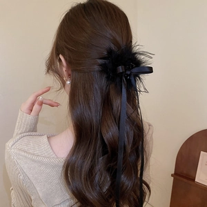 Detail view of a black ribbon bow hair clip with feathers worn by a female model
