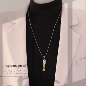 Detailed close-up of a colorful enamel koi fish pendant on a gold chain over a beige suit