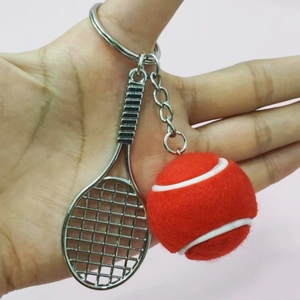Detail of creative red tennis ball and silver racket keychain pendant on a pink background