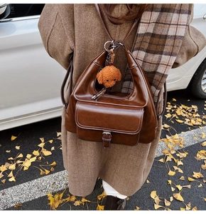 Close-up of brown oiled leather bag with white stitching and a cute dog plush charm