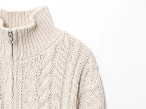 Detail of quarter-zip ribbed collar and chunky cable knit texture on beige sweater