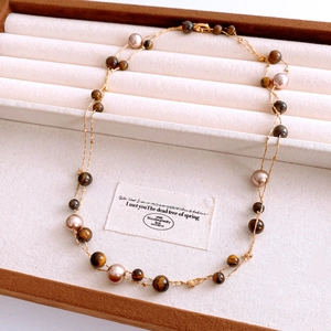 Detail of tiger eye and pearl double-layer gold necklace on a beige jewelry box