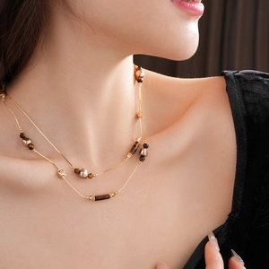 Nahaufnahme einer zweilagigen Goldkette mit Tigerauge-Steinen am Hals eines Models