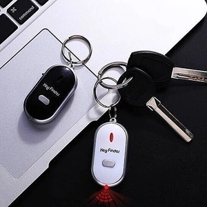 Black and white key finders with LED light indicator shown next to laptop and keys