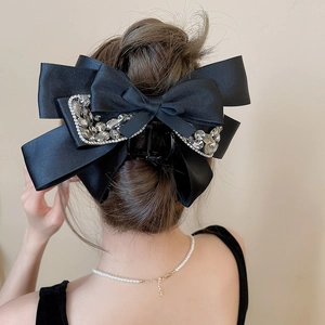 Detail of a large black satin bow hair claw clip with rhinestones worn by a model